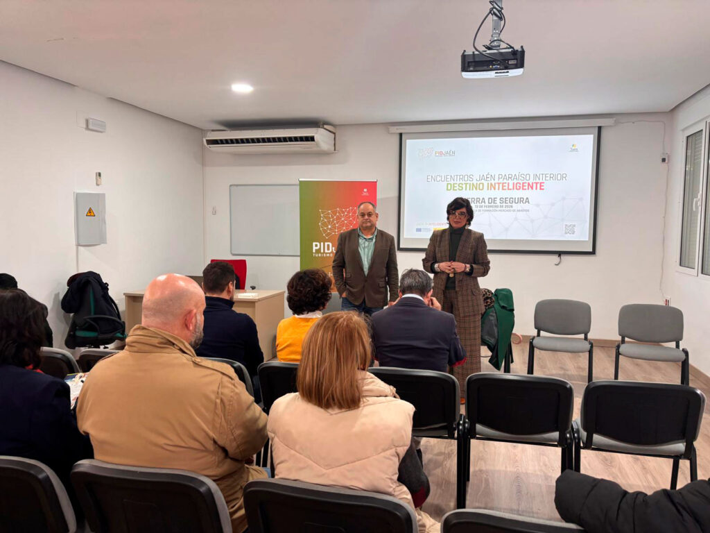 Dos ponentes presentan sobre turismo inteligente ante una audiencia en una sala de conferencias con proyección de diapositivas y logotipo PID Jaén visible