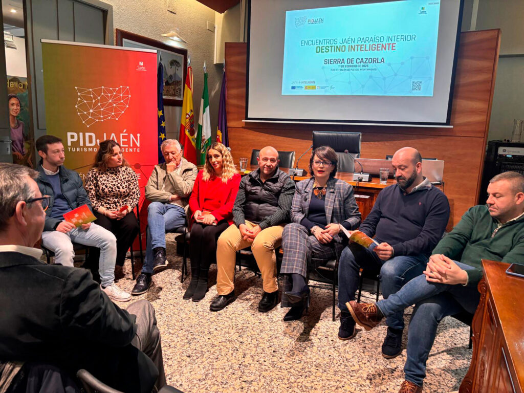 Grupo de personas reunidas en una sala de conferencias durante una jornada sobre Turismo Inteligente en la Sierra de Cazorla, con presentación sobre destino inteligente en pantalla de proyección