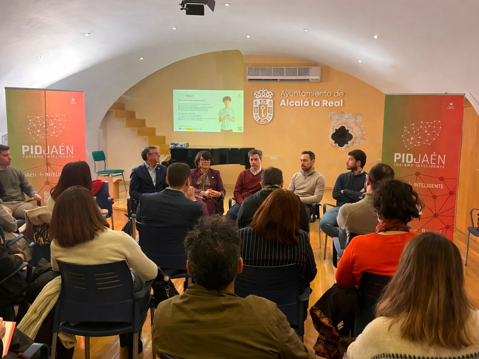 Ponentes en el escenario durante la presentación del proyecto PID Jaén en Alcalá la Real, con el logo de PID Jaén visible en el fondo